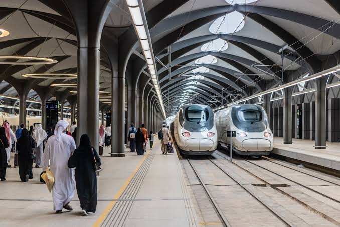 Umrah Transport Services: Best Rides in Makkah & Madinah Pilgrims walking near Haramain High-Speed Trains at a modern station in Saudi Arabia.